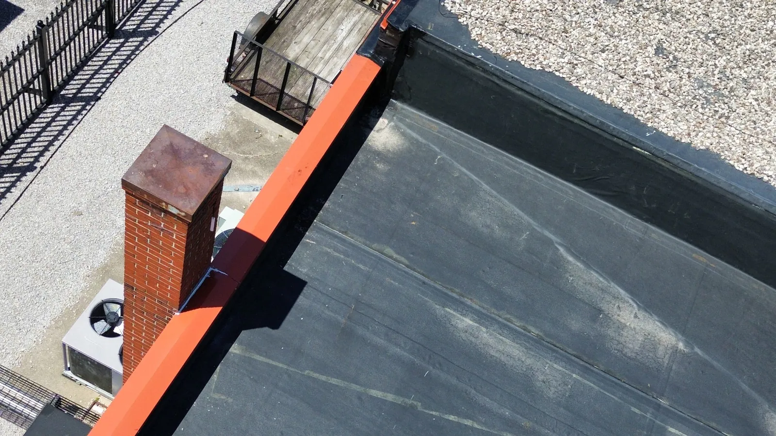 Aerial photograph of the roof edge with brick chimney, parapet coping, old EPDM surface and adjacent stone-ballasted roofing