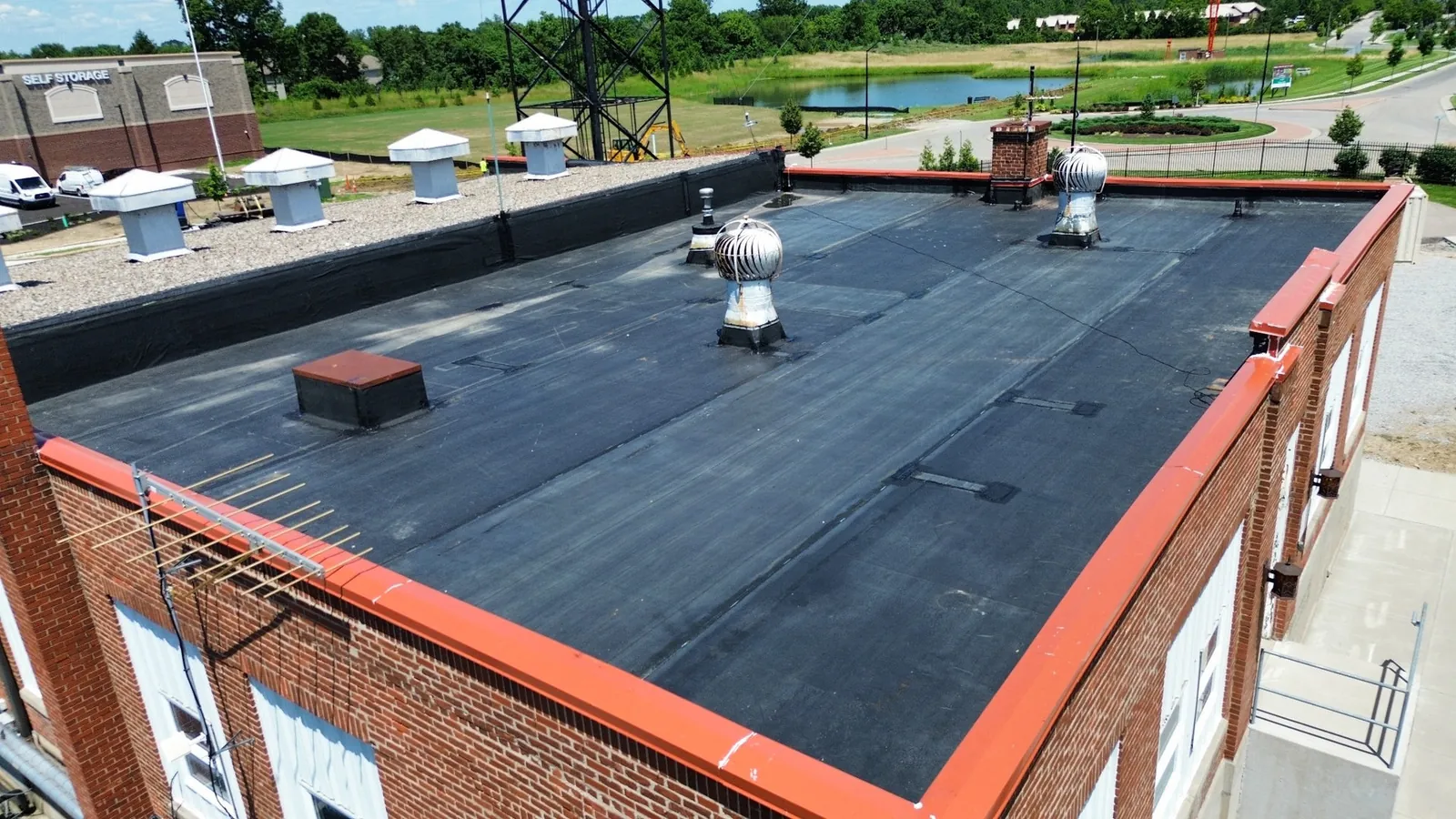 Drone view looking across aging black EPDM membrane on the brick transmitter building near the WLW tower